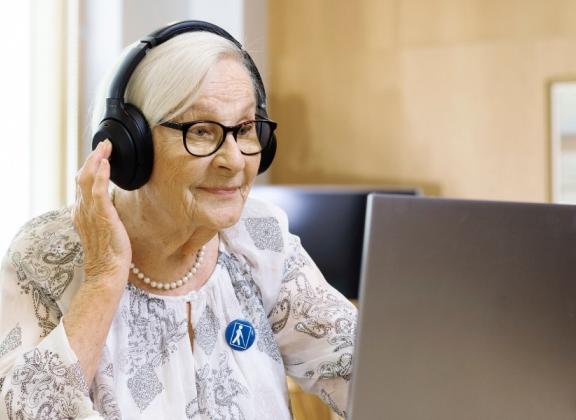 Seniorinainen tietokoneella luurit päässään.